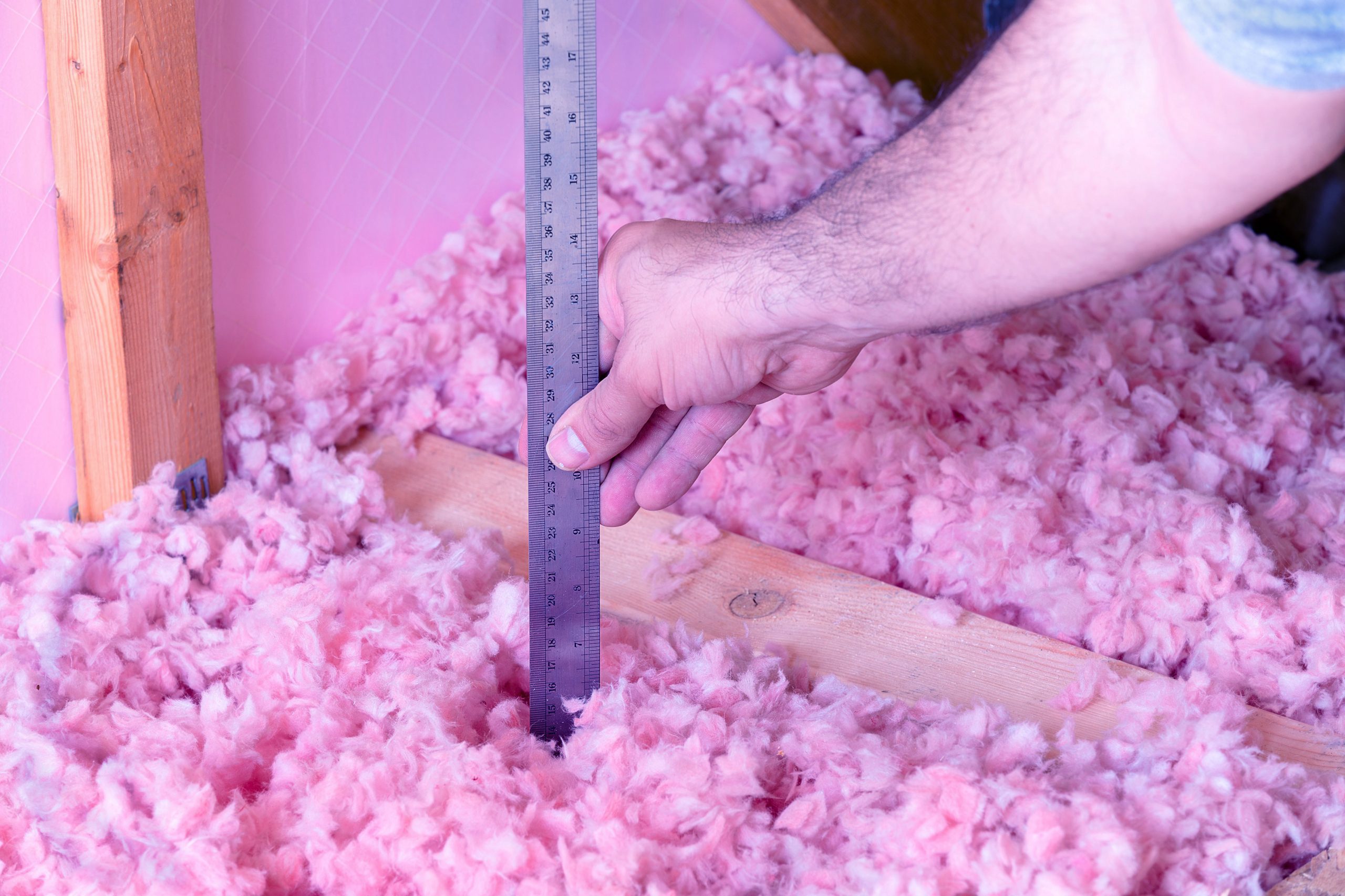 A contractor's arm holding up a ruler while conducting a blown-in fiberglass insulation project